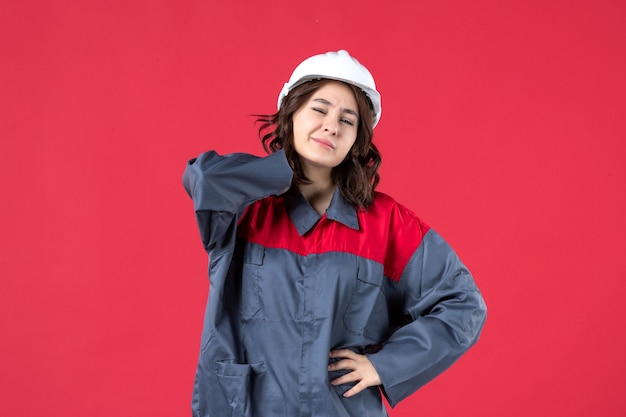 Bovenaanzicht van vrouwelijke bouwer in uniform met helm en leed aan hoofdpijn op geïsoleerde rode achtergrond