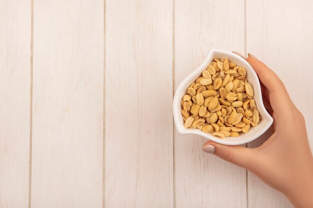 Bovenaanzicht van vrouwelijke hand met een kom met pijnboompitten op een beige houten tafel met kopie ruimte