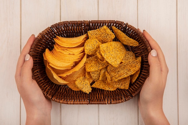 Bovenaanzicht van vrouwelijke handen met een emmer met knapperige chips op een beige houten tafel