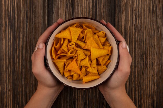 Gratis foto bovenaanzicht van vrouwelijke handen met een kom kegelvorm maïs snacks op een houten tafel