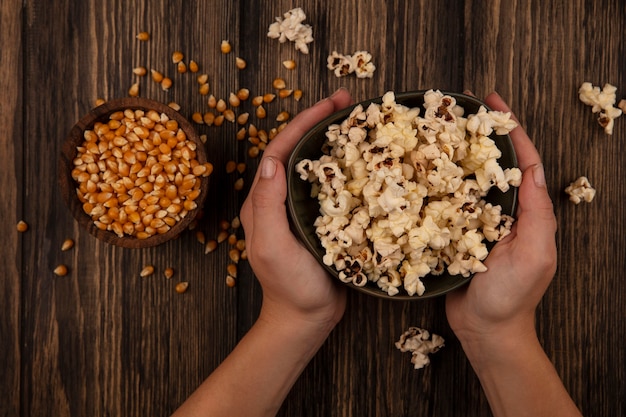 Bovenaanzicht van vrouwelijke handen met een kom popcorn met maïskorrels op een houten kom op een houten tafel