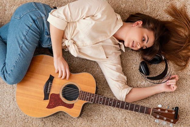 Bovenaanzicht van vrouwelijke muzikant thuis op de verdieping met koptelefoon en akoestische gitaar