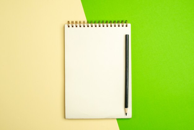 Bovenaanzicht van wit notitieboekje met pen op witte en gele achtergrond