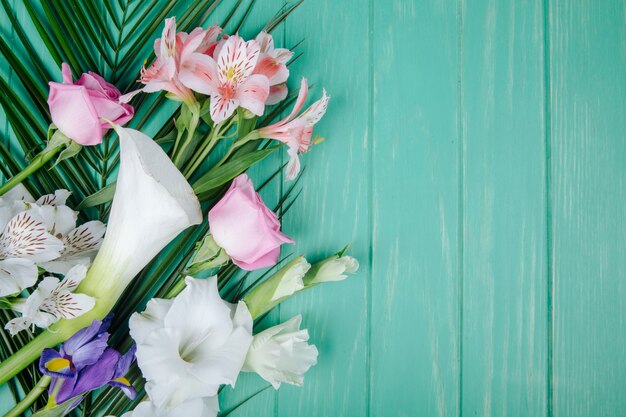 Bovenaanzicht van witte kleur calla lelies en gladiolen met donkerpaarse iris en roze rozen en alstroemeria bloemen op palmblad op groene houten achtergrond met kopie ruimte