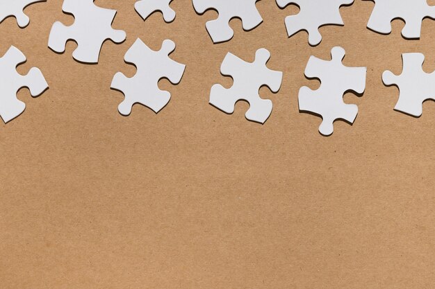 Bovenaanzicht van witte puzzelstukjes op bruin papier textuur