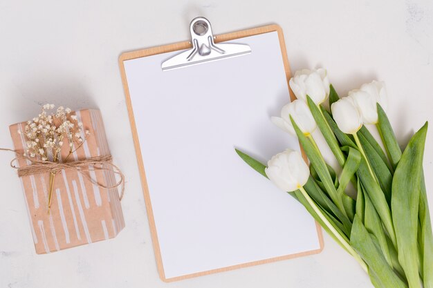 Bovenaanzicht van witte tulp bloemen; geschenkdoos en klembord op witte achtergrond
