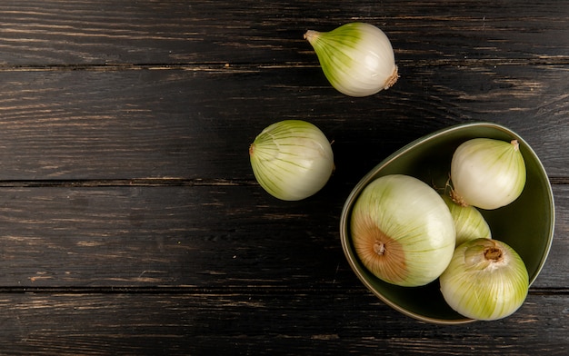 Gratis foto bovenaanzicht van witte uien in kom op houten achtergrond met kopie ruimte