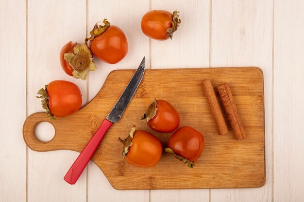 Bovenaanzicht van zachte dadelpruimen op een houten keukenplank met kaneelstokjes met mes op een wit houten oppervlak