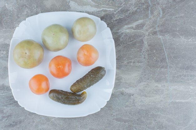 Bovenaanzicht van zelfgemaakte augurk. onrijpe tomaten en komkommer op witte plaat.