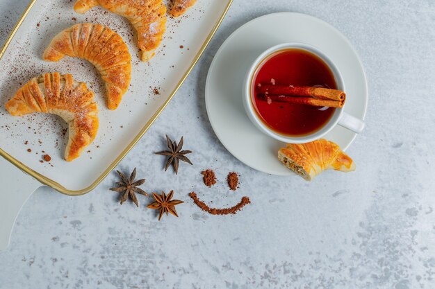 Bovenaanzicht van zelfgemaakte croissants met verse thee op grijze ondergrond.