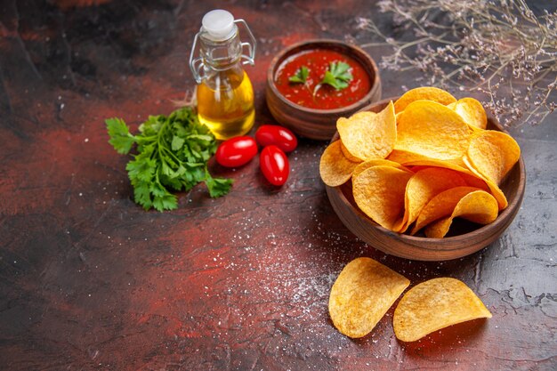 Bovenaanzicht van zelfgemaakte heerlijke aardappelkrokante chips in een kleine bruine kom oliefles groene tomatenketchup op donkere tafel