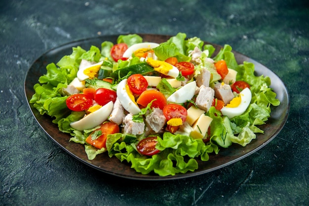 Bovenaanzicht van zelfgemaakte heerlijke salade met veel ingrediënten in een plaat op zwarte groene mix kleuren achtergrond