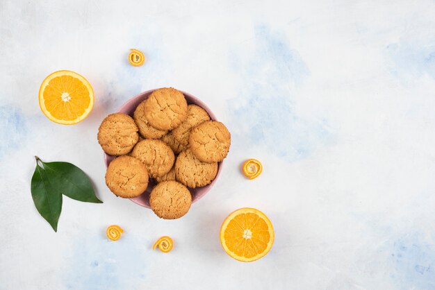 Bovenaanzicht van zelfgemaakte koekjes met half gesneden sinaasappel over witte tafel.