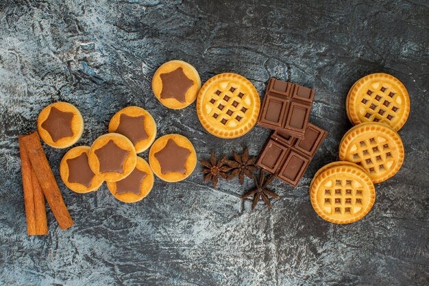 Bovenaanzicht van zoete koekjes met chocoladerepen en kaneelstokjes op grijze grond