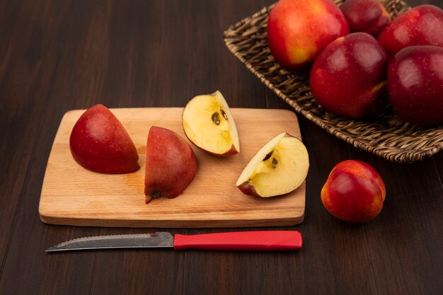 Bovenaanzicht van zoete rode appels op een rieten dienblad met appelschijfjes op een houten keukenbord met mes op een houten muur