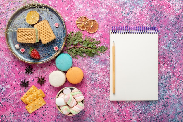 Bovenaanzicht van zoete wafels met macarons op lichtroze oppervlak