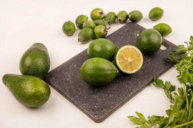 Bovenaanzicht van zure limoenen op een bord van de keuken met feijoas en avocado's geïsoleerd op een witte muur