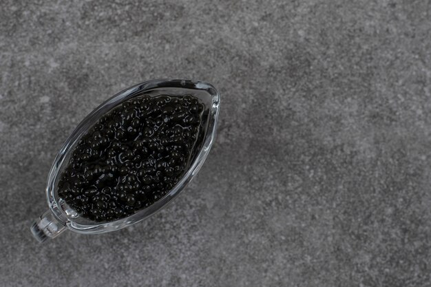 Bovenaanzicht van zwarte kaviaar. Kaviaar in glazen kom over grijze tafel.