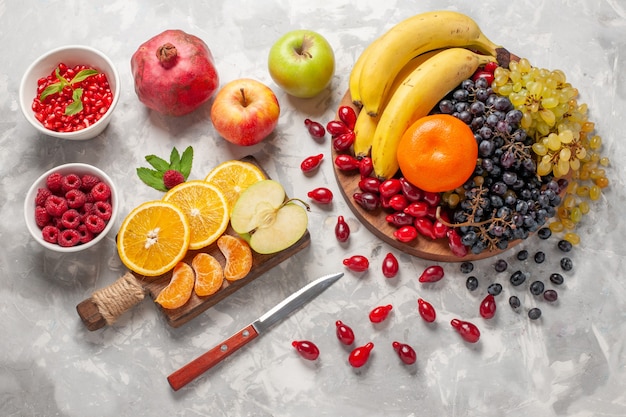 Gratis foto bovenaanzicht vers fruit samenstelling bananen kornoeljes en druiven op licht-wit oppervlak fruit bes versheid vitamine