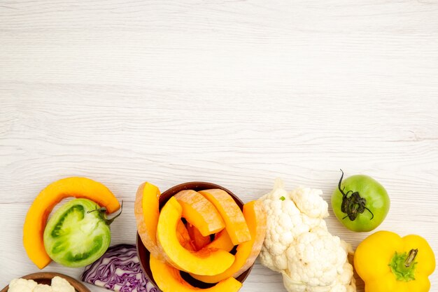 Bovenaanzicht vers gesneden groenten pompoen in kom groene tomaten rode kool paprika bloemkool op witte houten oppervlak met vrije ruimte