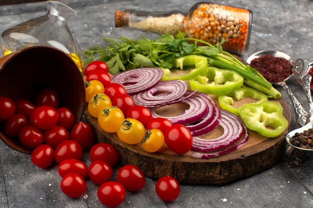 bovenaanzicht vers gesneden groenten zoals uien, groene paprika en tomaten op de grijze