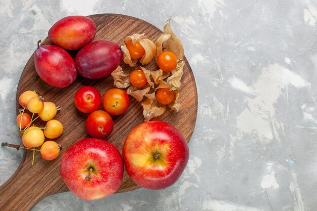 Bovenaanzicht verschillende gevormde pruimen zuur en vers fruit met kersen op het lichte witte bureau.