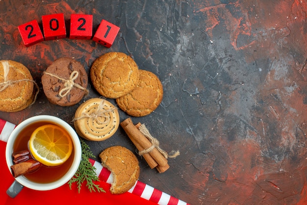 Bovenaanzicht verschillende koekjes vastgebonden met touw kopje thee kaneelstokjes houtblokken op donkerrode tafel met vrije plaats