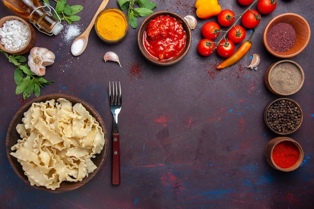 Bovenaanzicht verschillende kruiden met verse tomaten en deeg op donkere ruimte