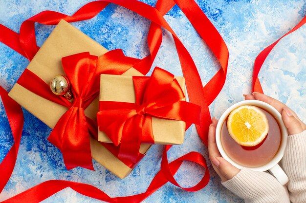 Bovenaanzicht verschillende maten geschenken gebonden met rood lint kopje thee in vrouwelijke hand op blauw witte tafel