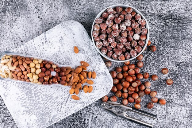 Bovenaanzicht verschillende noten in volle fles noten en kom met notenkraker en pecannoot, pistachenoten, amandel, pinda, cashew, pijnboompitten
