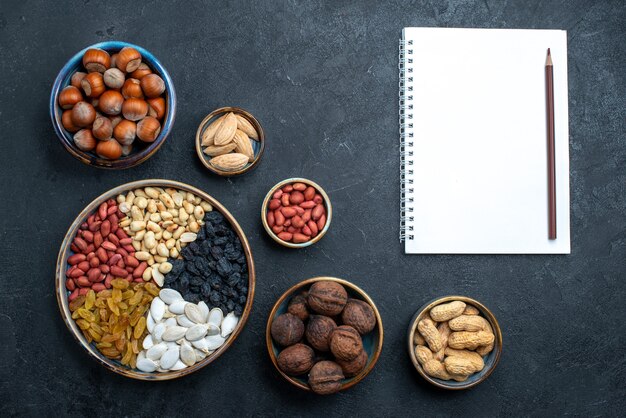 Bovenaanzicht verschillende noten samenstelling van snacks met blocnote op donkergrijze achtergrond noot snack foto walnoot hazelnoot