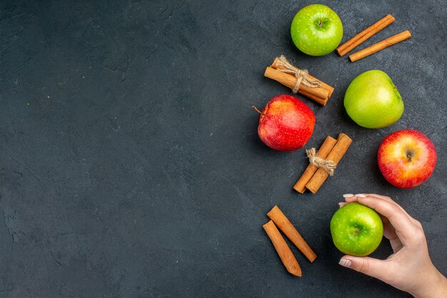 Bovenaanzicht verse appels kaneelstokjes appel in vrouwelijke hand op donkere oppervlakte vrije ruimte