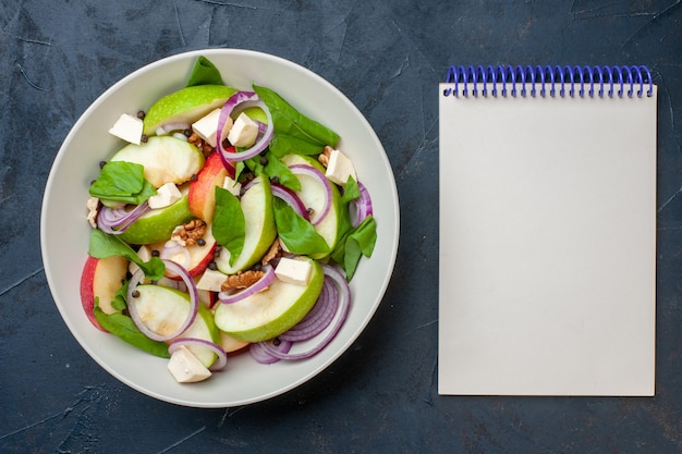 Bovenaanzicht verse appelsalade in kom notitieboekje op donkerblauwe achtergrond