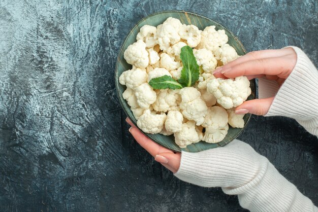 Bovenaanzicht verse bloemkool in plaat in vrouwelijke handen op de lichtgrijze tafel