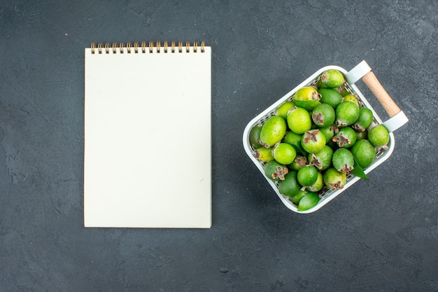 Bovenaanzicht verse feijoas op plastic mand notebook op donkere ondergrond