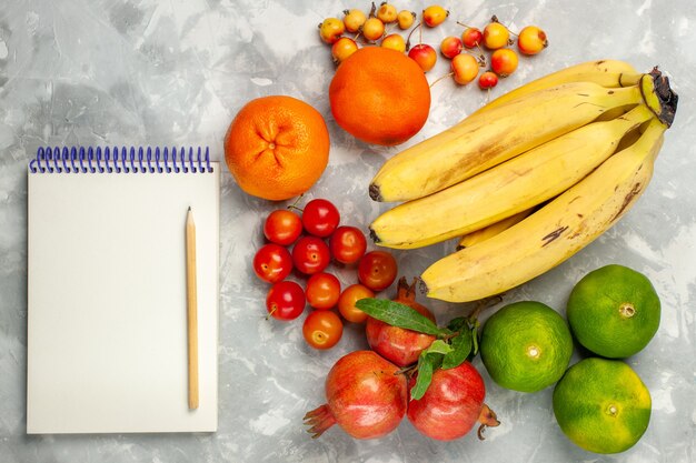 Bovenaanzicht verse gele bananen met granaatappels Kladblok en mandarijnen op lichtwit bureau