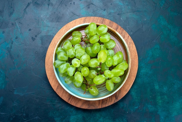 Bovenaanzicht verse groene druiven, zacht sappig fruit in plaat op het donkerblauwe bureau.