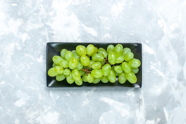 Gratis foto bovenaanzicht verse groene druiven zacht sappig fruit in zwarte vorm op het lichtbureau.