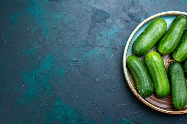 Bovenaanzicht verse groene komkommers rijpe groenten in plaat op het donkerblauwe bureau.