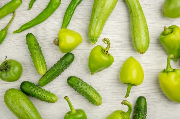 Bovenaanzicht verse groene paprika's met groene komkommers en tomaten op wit bureau kleur rijpe salade foto maaltijd hot