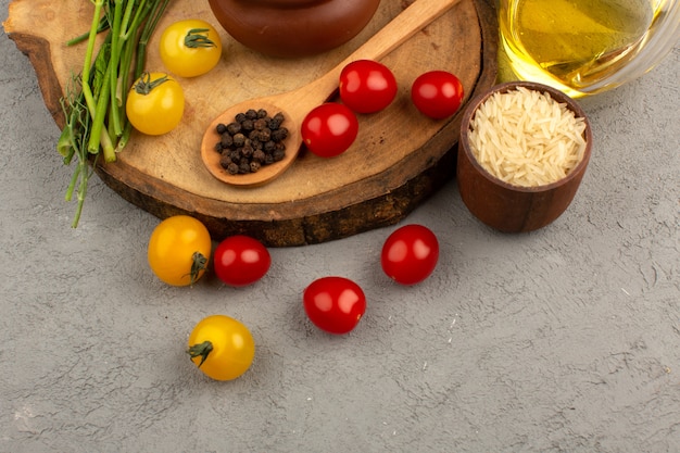 Bovenaanzicht verse groenten geheel zoals gele en rode tomaten samen met olijfolie op de grijze