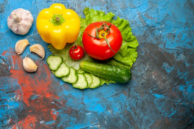Bovenaanzicht verse groenten komkommer tomaat groene salade en knoflook op blauwe achtergrond