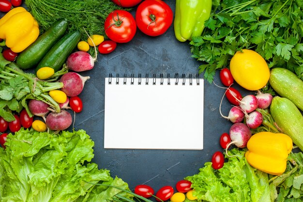 Bovenaanzicht verse groenten tomaten sla radijs citroen courgette peterselie cherry tomaten Kladblok in het midden op een donkere ondergrond