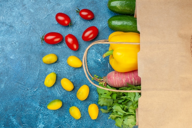 Gratis foto bovenaanzicht verse groenten verspreid uit papieren zak cherrytomaatjes cumcuat peterselie radijs komkommer paprika op blauwe tafel