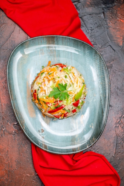 Bovenaanzicht verse groentesalade binnen bord met rood weefsel op donkere tafel