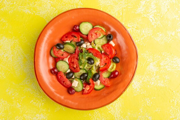 Bovenaanzicht verse groentesalade met gesneden komkommers tomaten olijf binnen plaat op het gele bureau groente voedselsalade maaltijd kleur