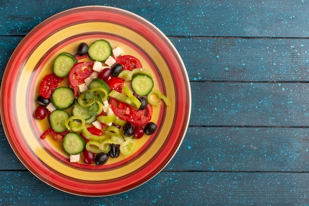 Bovenaanzicht verse groentesalade met gesneden komkommers, tomaten, olijven en witte kaas binnen plaat met tomaten op de donkerblauwe achtergrond Groente voedselsalade maaltijd