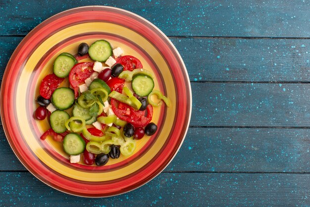 Bovenaanzicht verse groentesalade met gesneden komkommers, tomaten, olijven en witte kaas binnen plaat met tomaten op de donkerblauwe achtergrond Groente voedselsalade maaltijd