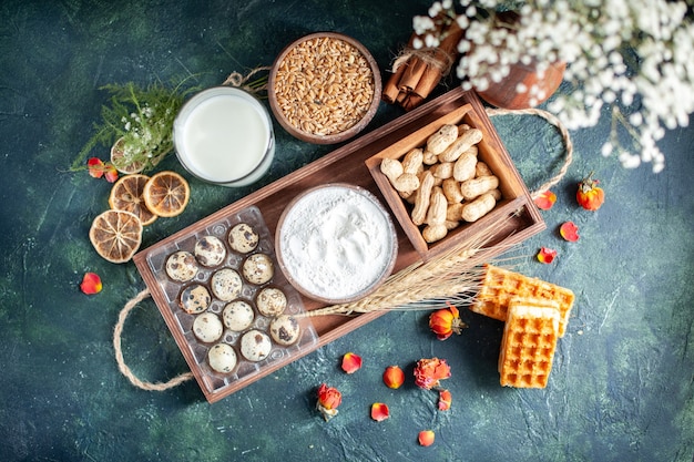 Bovenaanzicht verse melk met koekjes, noten en eieren op donkerblauwe achtergrond deeg bak cake biscuit taart thee broodje gebak suiker