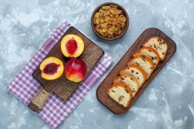 Bovenaanzicht verse perziken zacht en smakelijk fruit met taarten en rozijnen op het lichtwitte bureau